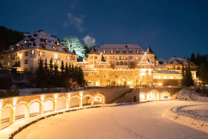 Das Hotel Kitzbühel abends erleuchtet, umgeben von schneebedeckter Winterlandschaft und Bergen. 