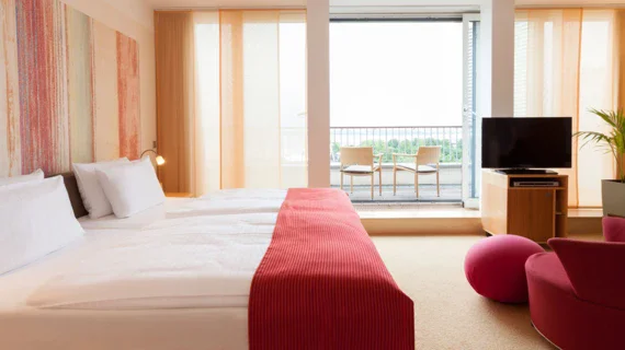 Ein Hotelzimmer mit einem großen Bett, einem roten Sessel und einem Balkon mit Meerblick.