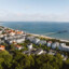 Aussicht auf eine Stadt am Wasser mit Bäumen und Gebäuden unter einem bewölkten Himmel.