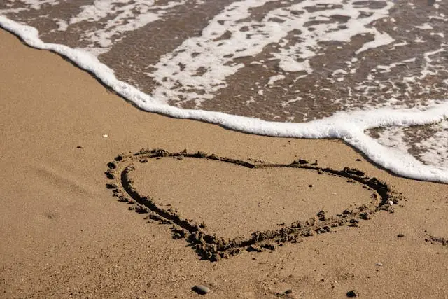 Herz im Sand neben einer Welle am Strand