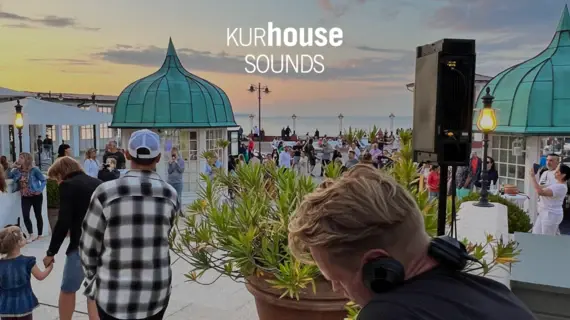 Stimmungsvolle Abendveranstaltung ‚Kurhouse Sounds‘ mit DJ, tanzenden Gästen und Blick auf die Ostsee.