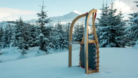 Ein Schlitten steht in einer verschneiten Winterlandschaft und im Hintergrund sind Berge zu sehen.