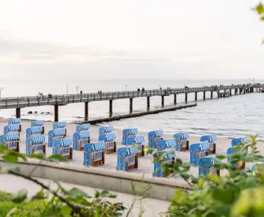 Strandkörbe und ein Pier am Wasser unter bewölktem Himmel