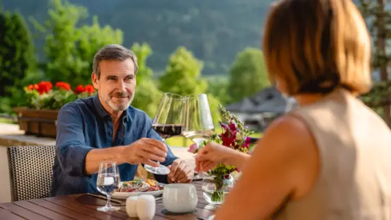 Ein Mann und eine Frau sitzen an einem Tisch im Freien und trinken Wein.