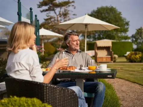 Ein Mann und eine Frau sitzen an einem gedeckten Frühstückstisch im Freien.