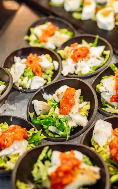 Ein appetitlich angerichtetes Buffet mit kleinen Portionen von Salat mit Fisch und rotem Kaviar in schwarzen runden Schalen. 