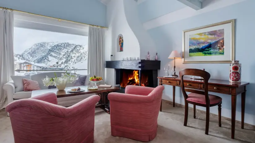 A cozy hotel room with a fireplace and red armchairs.