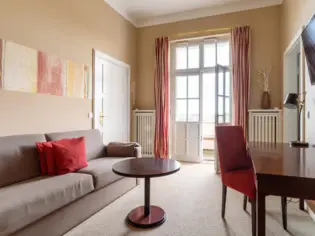 Ein Wohnbereich in einem Hotelzimmer mit einem braunen Sofa mit drei roten Kissen sowie einem Schreibtisch.