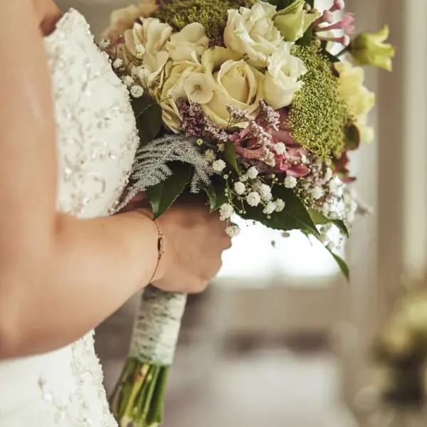 Braut in einem Hochzeitskleid hält einen Blumenstrauß.