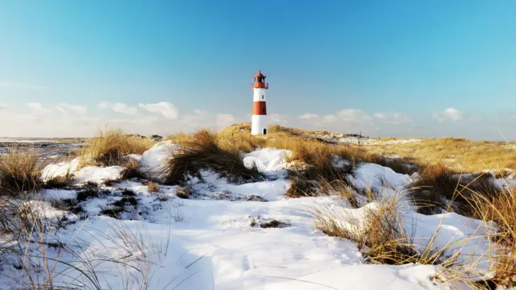 Leuchtturm im Schnee mit sichtbarem Gras und winterlicher Landschaft.