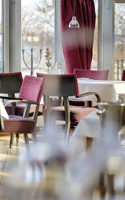 Elegant gedeckter Tisch in einem Restaurant mit Tischdecke, Geschirr, Weingläsern und einem Blumengesteck.