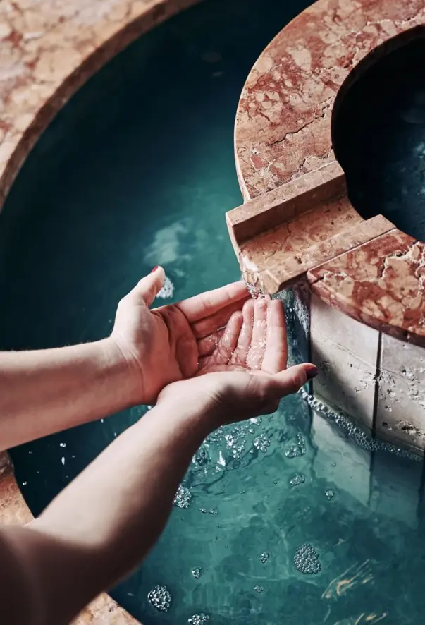 Aus einem Brunnen läuft Wasser über die Hände einer Person. 