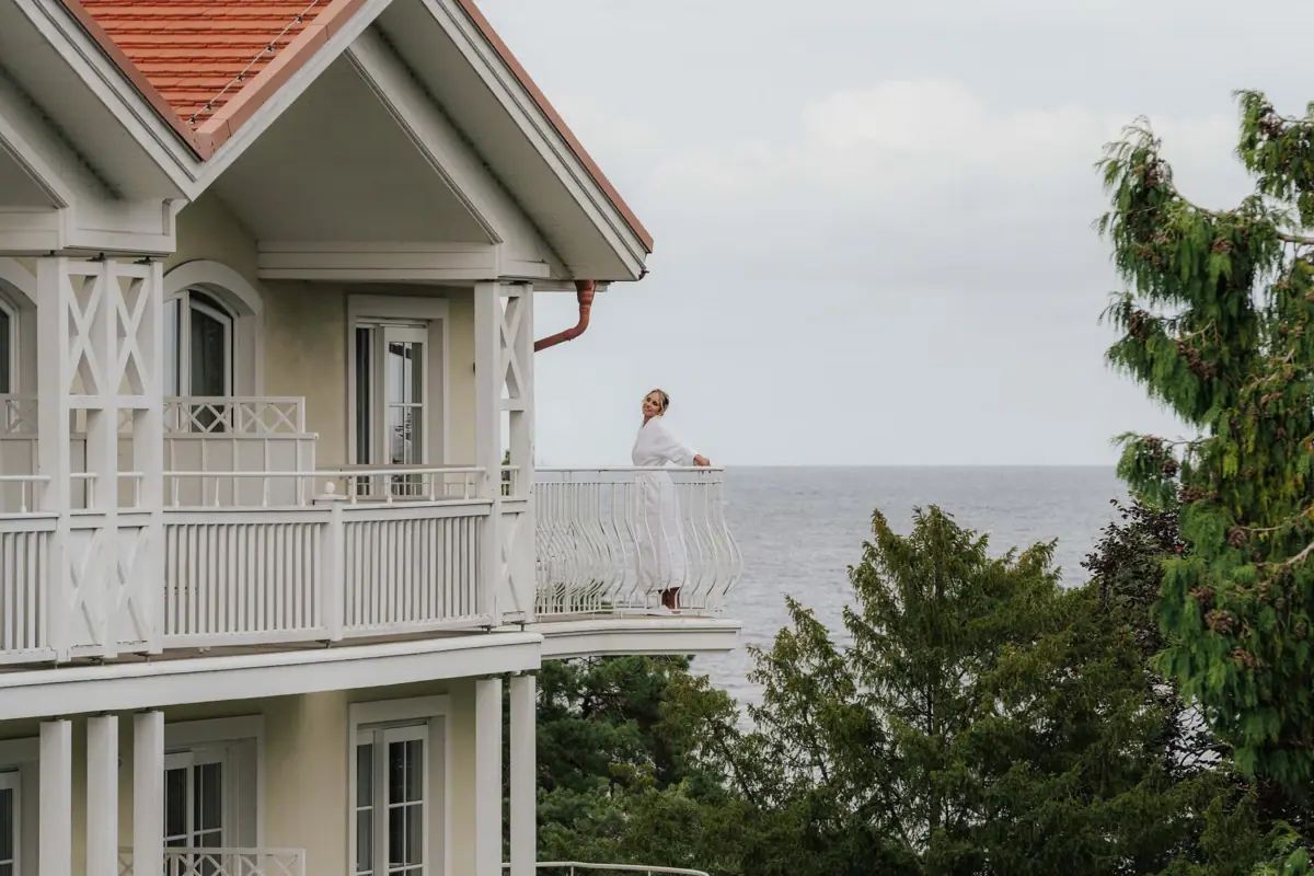 Eine Frau steht auf einem Balkon mit Blick auf ein Gewässer.