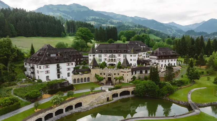 Das A-ROSA Kitzbühel mit einem Teich und einem Golfplatz, umgeben von Bäumen und einer weiten Berglandschaft.