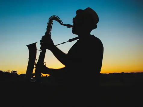 Silhouette eines Mannes, der im Freien bei Sonnenuntergang Saxophon spielt.