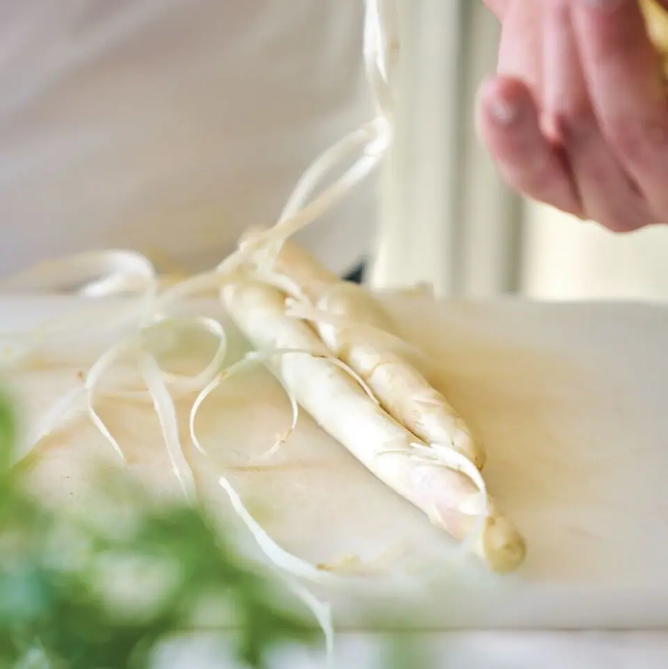 Eine Person schält ein Stück weißen Spargel.