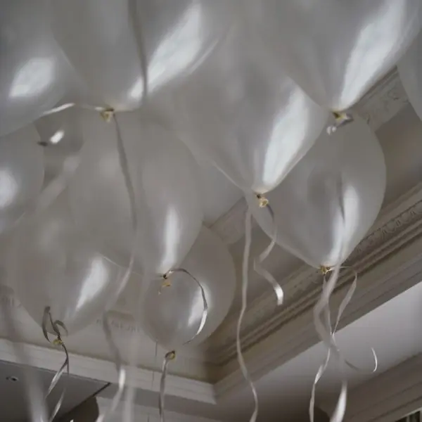 An der Decke sammeln sich viele helle Luftballons mit silbernen Schnur. 