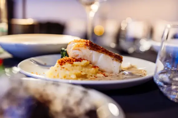 Ein Teller mit Essen auf einem Tisch, umgeben von Tafelgeschirr und einem Weinglas.