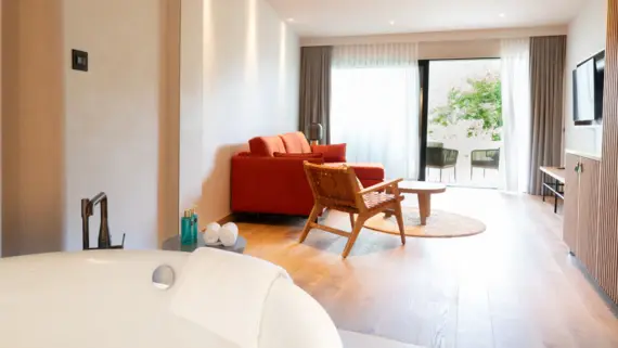 Ein elegant eingerichtetes Hotelzimmer mit einer Badewanne und einem Sofa mit Blick auf eine Terrasse mit Sitzgelegenheiten..