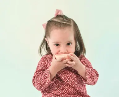 A little girl in a red floral dress is eating something.