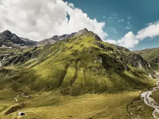 Grüne Berglandschaft mit grasbewachsenen Flächen und vereinzelten Wolken.