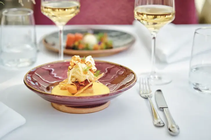 Ein Teller mit Essen auf einem Tisch, umgeben von Weingläsern und Besteck.