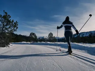 Skilangläuferin auf verschneiter Straße vor einer Bergkulisse.