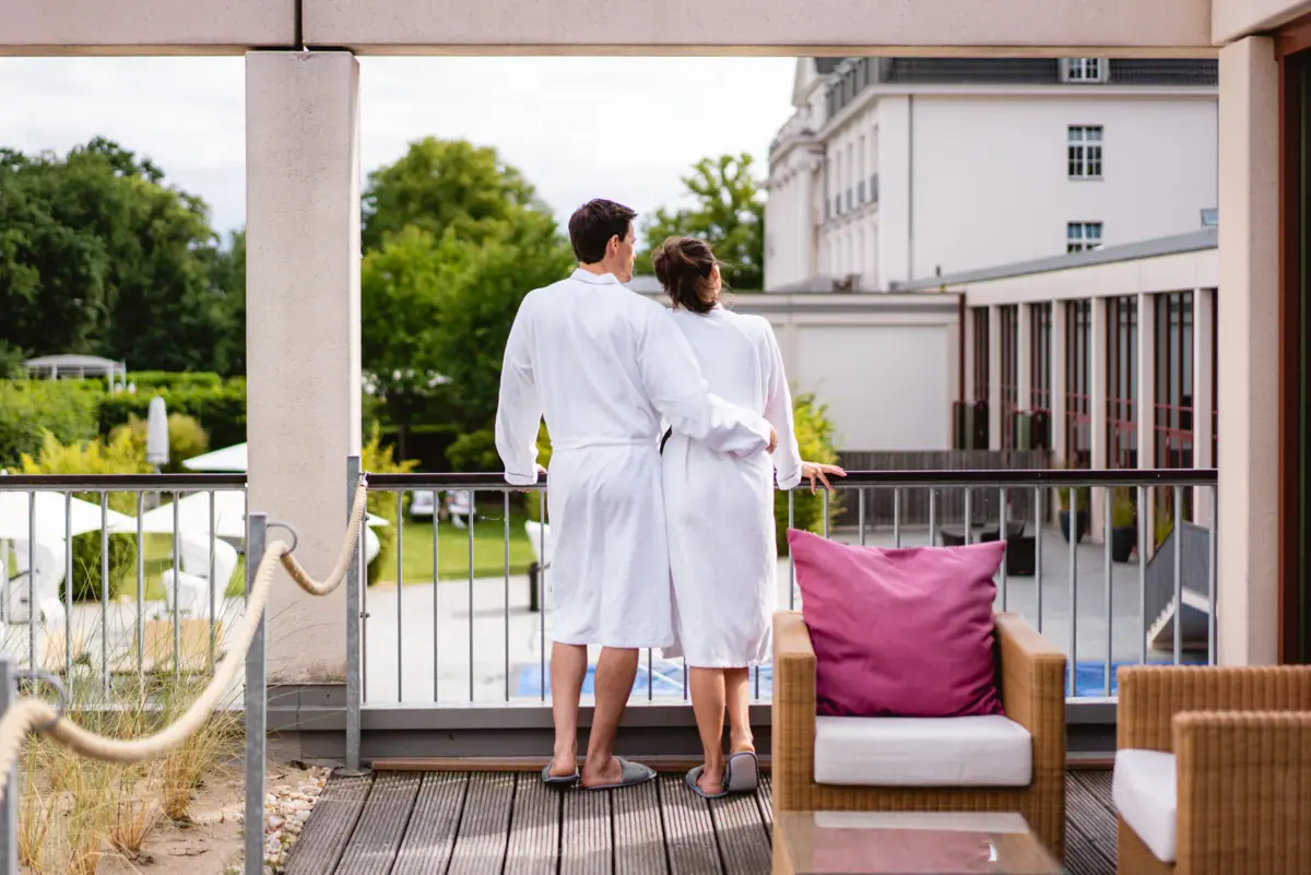 Ein Mann und eine Frau in weißen Bademänteln stehen auf einem Balkon.