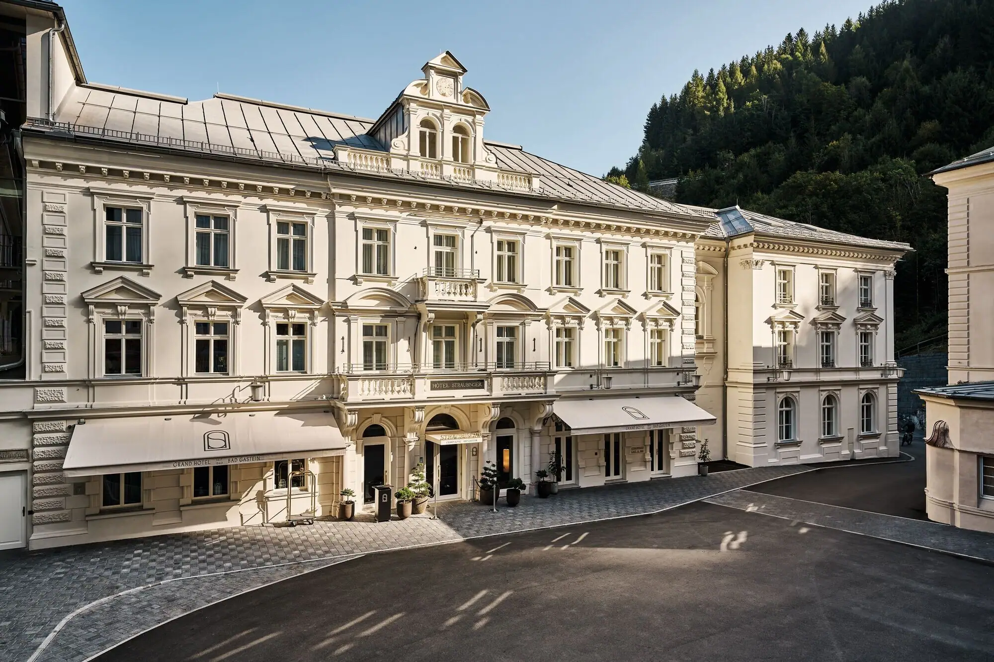 Großes weißes Gebäude mit Fenstern und gepflastertem Bereich im Vordergrund.