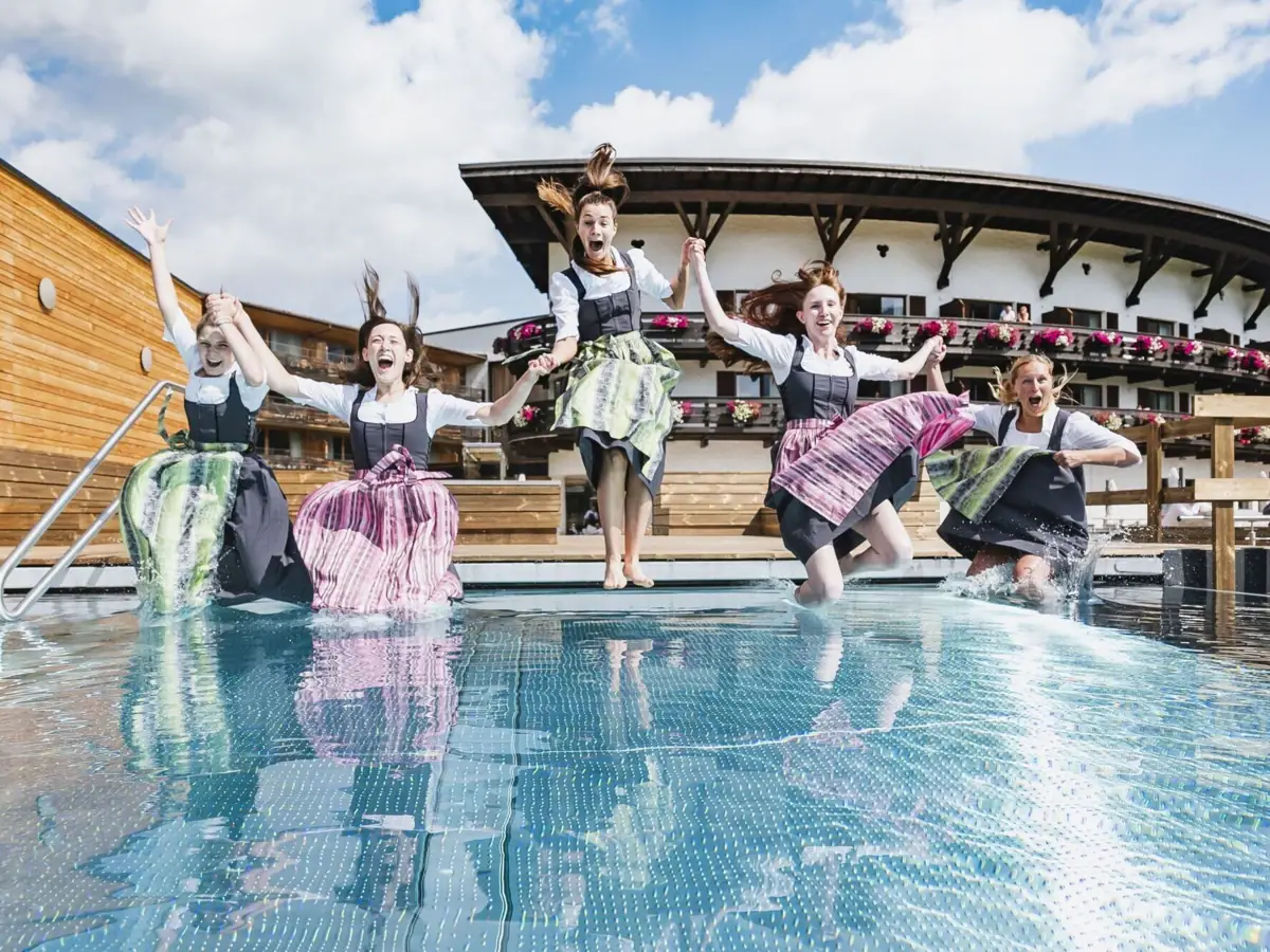 Mitarbeiter Kleinwalsertal Eine Gruppe von Frauen mit Dirndln springt in einen Pool.