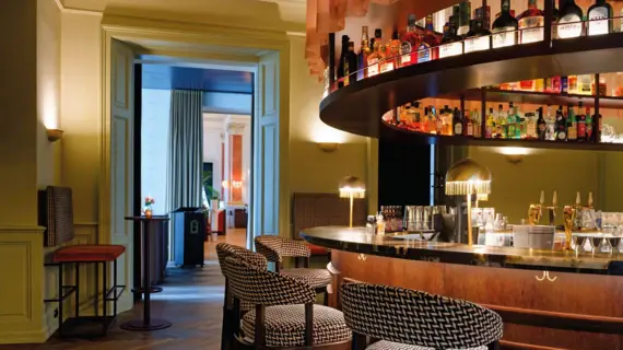 Elegante Hotelbar im Straubinger Grand Hotel Bad Gastein mit stilvollen Barhockern, goldenen Lampen und einer großen Auswahl an Spirituosen in gemütlicher Atmosphäre.
