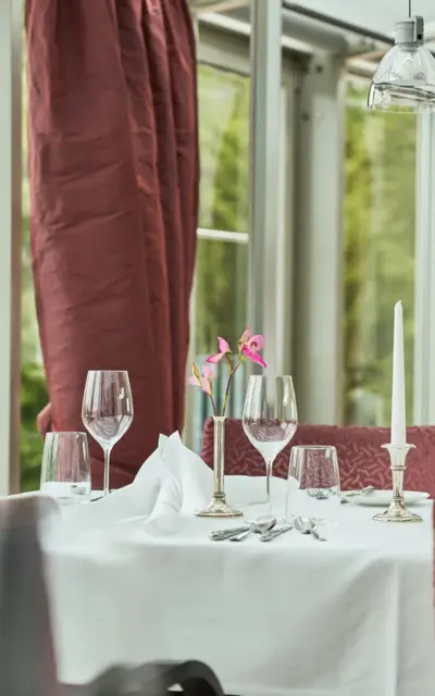 Elegant gedeckter Tisch in einem Restaurant mit Tischdecke, Geschirr, Weingläsern und einem Blumengesteck.