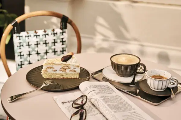 Ein Tisch mit einem Kaffee, einem Stück Torte, einer Zeitung und Lesebrille.