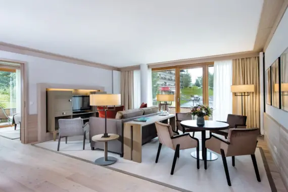 Living room with table and chairs, light wooden floor and large windows.