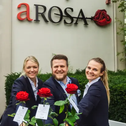 Gruppe von Personen in Anzügen und mit roten Rosen in der Hand lächelt im Freien.