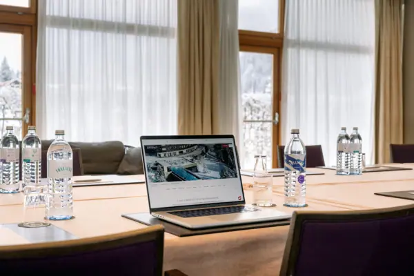 Laptop auf einem Tisch mit Wasserflaschen und einem Fenster im Hintergrund.