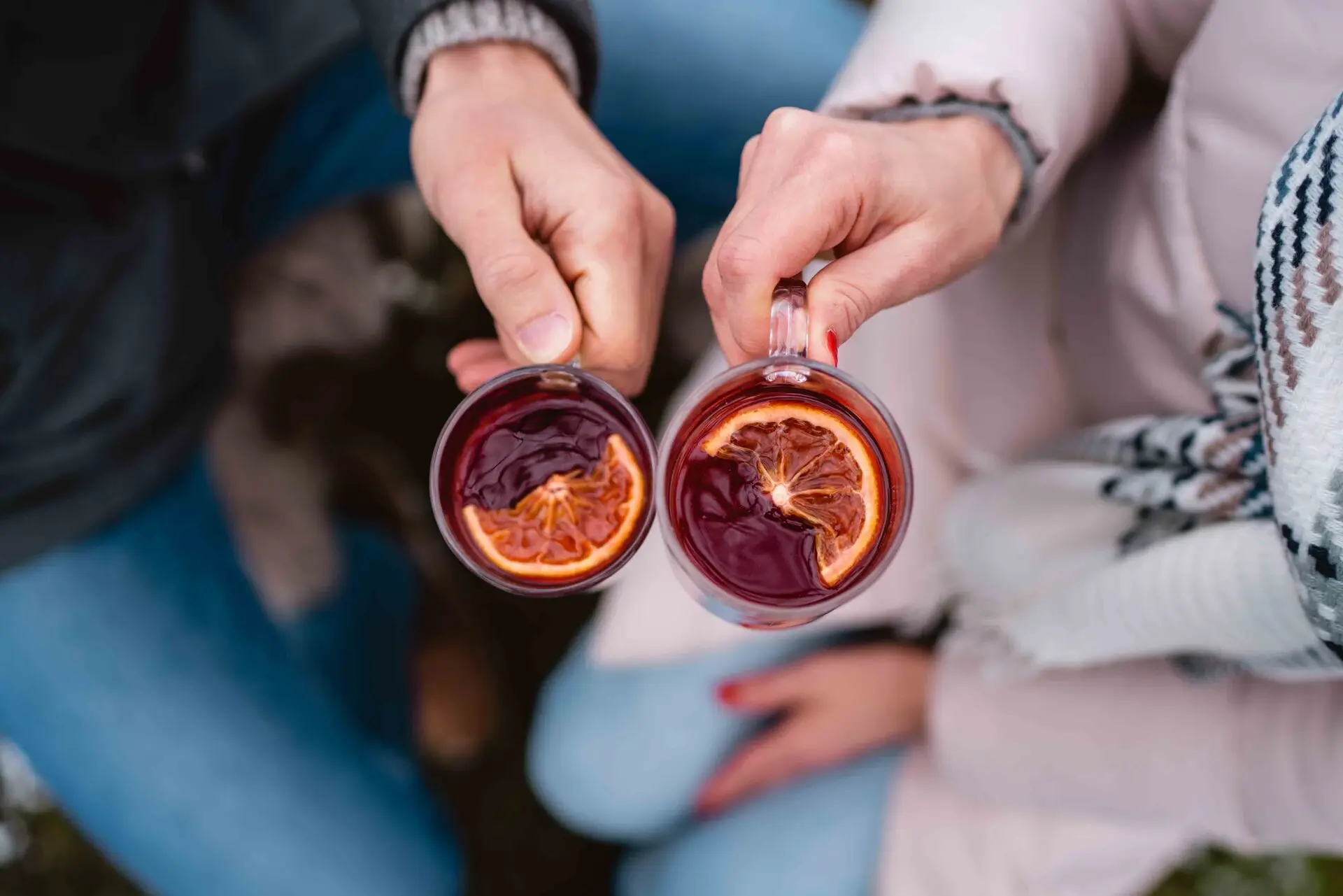 Hände eines Paares, die Gläser mit roter Flüssigkeit und Orangenscheiben halten