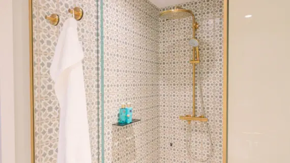 Gold shower head with white towel in a tiled bathroom.