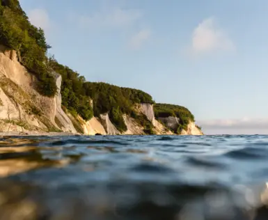 Blick auf eine Klippe mit Bäumen an einem Gewässer.