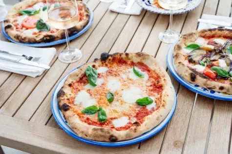 Diversi piatti con pizza e bicchieri di vino su un tavolo di legno.