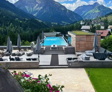 Luftanischt eines Außenpools mit Blick auf Berge und umstehenden Liegen. 