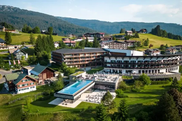 Gebäude mit einem Infinity-Pool inmitten eines Bergdorfes, umgeben von Bäumen und einer Landschaft mit Bergen.