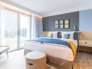Ein modernes Hotelzimmer mit einem großen Bett und einer blau-gelben Tagesdecke.