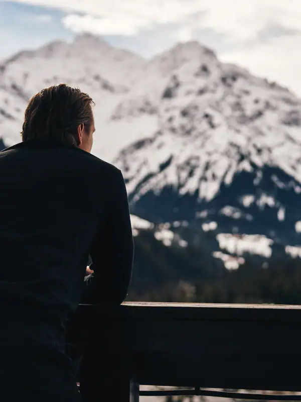 Ein Mann lehnt an einem Geländer mit Blick auf einen verschneiten Berg.