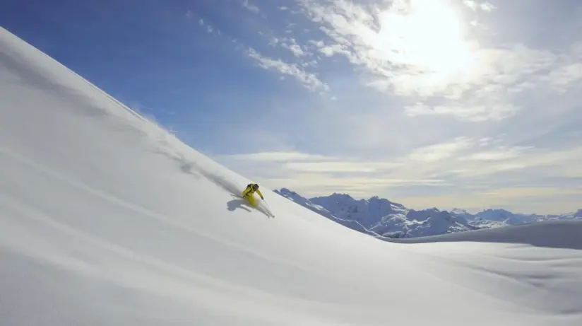 A skier in yellow clothing is skiing down a steep slope.