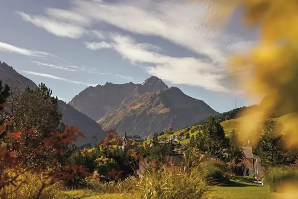 Herbstliche Landschaft mit Berg im Hintergrund, umgeben von Gras und vereinzelten Bäumen.