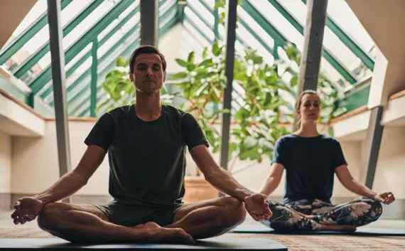 Ein Mann und eine Frau sitzen lächelnd auf Yogamatten.