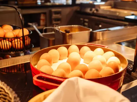 Im Fokus steht ein runder Topf an gekochten Eiern. Im Hintergrund ist eine offene Küche zu sehen. 