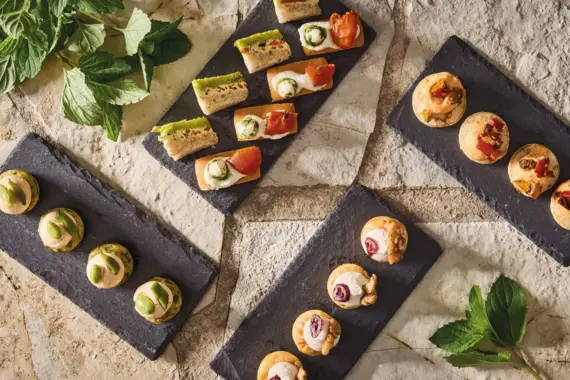 Eine Auswahl an Fingerfood auf Schieferplatten angerichtet, inklusive Canapés und kleinen Snacks.