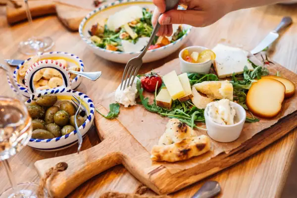 Gastronomie Ein Holzbrett mit Käse, eine Schale mit Oliven und einer Gabel.